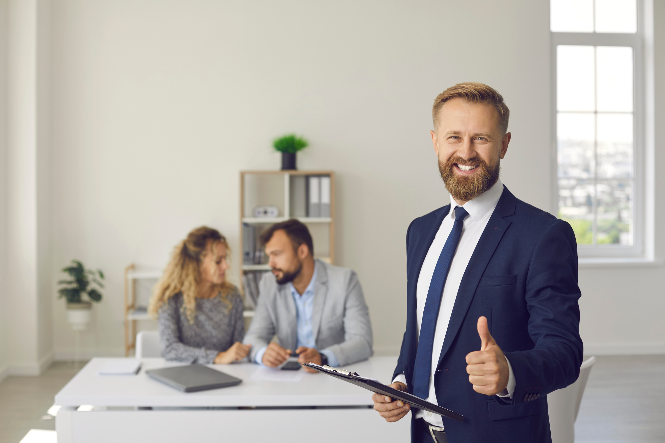 Happy Real Estate Agent or Mortgage Broker Standing in Office, Smiling and Giving Thumbs up